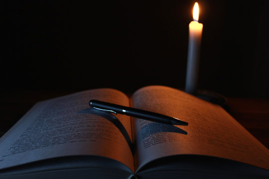 an open book with a pen laying on it and a candle shining on the book