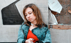 a despondent-looking young womand sitting against a wall